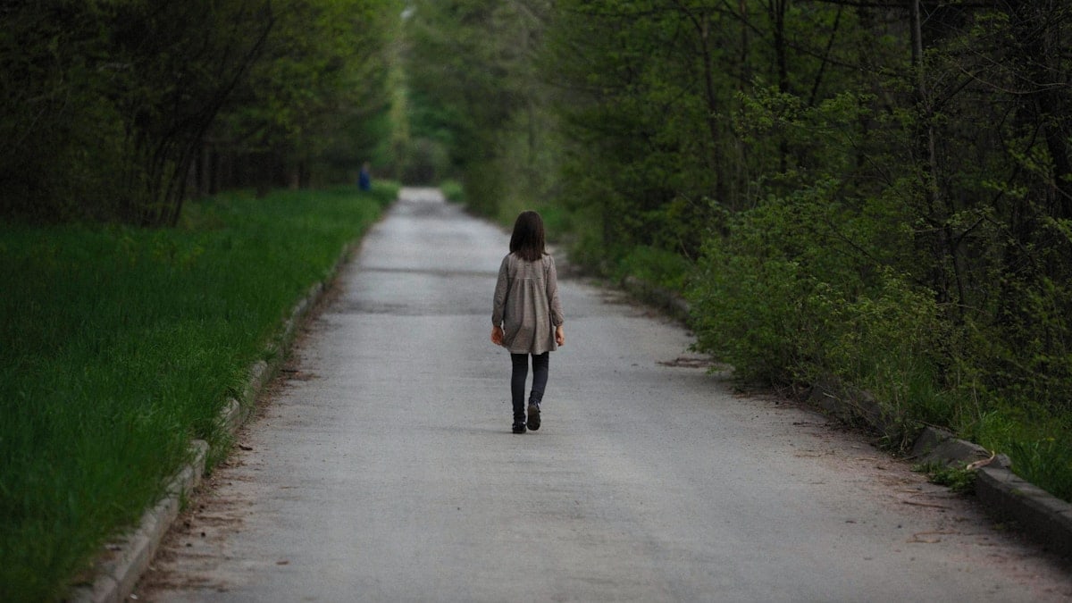 a woman walking down a road in the middle of a forest